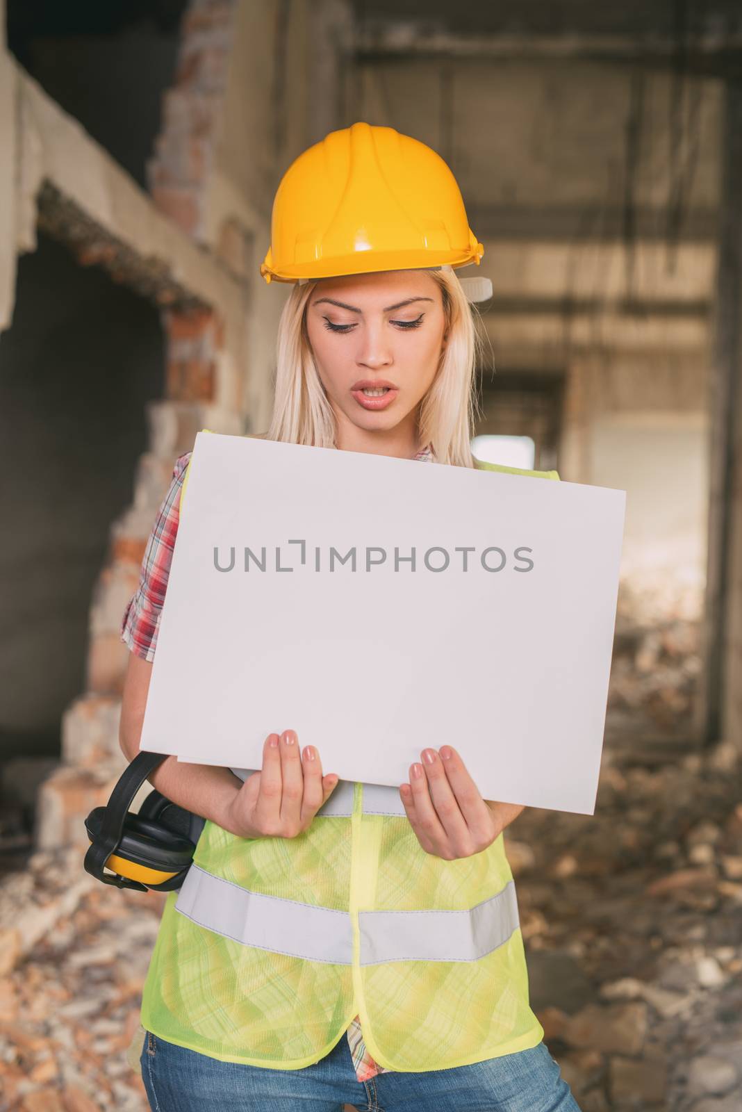Beautiful young female construction architects holding a blank white board in building damaged in the disaster. 