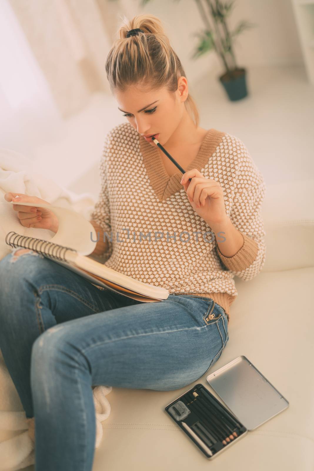 Beautiful young woman relaxing by drawing in a sketchbook with color pencils at home. 
