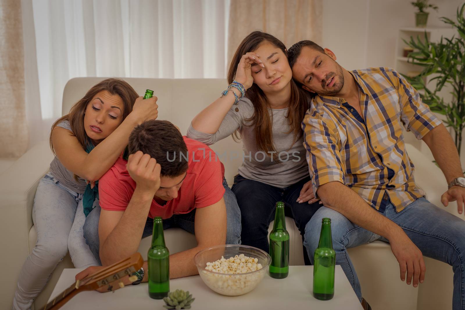 Four young friends drunk and hungover after house party sitting on the couch.