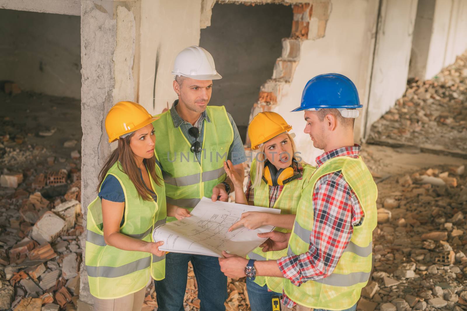 Four construction architects review plan in front building damaged in the disaster.