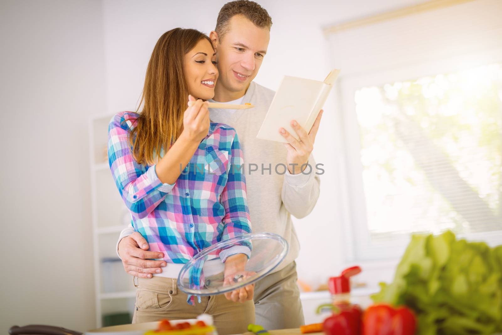 Beautiful young couple cooking healthy meal in the domestic kitchen. They reading recipe in the cookbook.