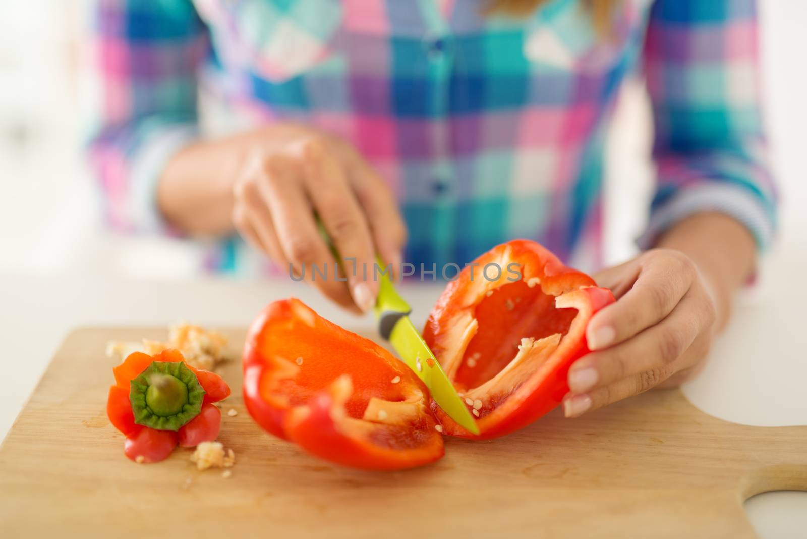 Close-up of a female hands cutting red paprika on the kitchen board.
