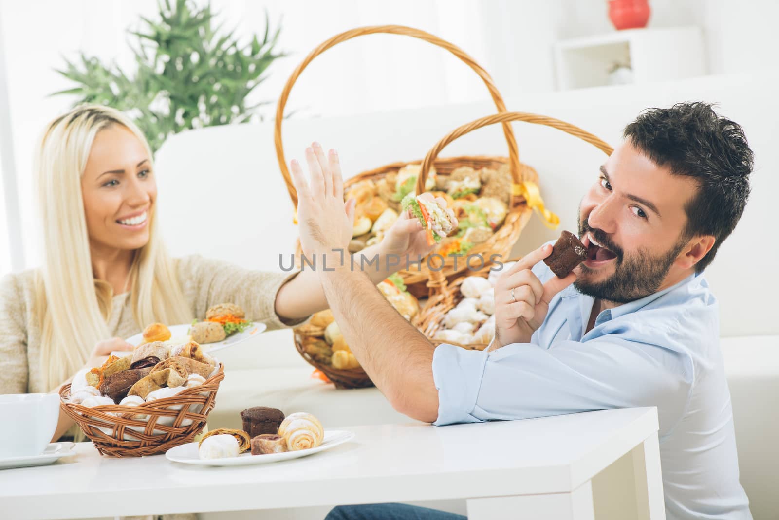 Beautiful young couple eat pastries. Beside them are woven baskets full of salty and sweet pastries. Selective focus.