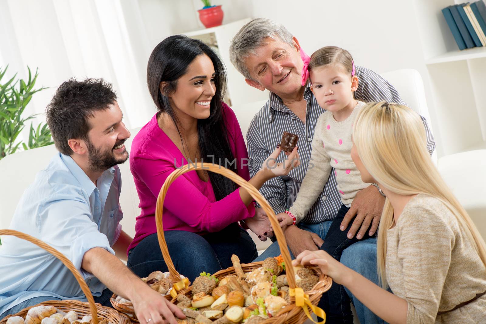 Happy family in their home eating pastries from beautifully decorated woven baskets that are on the table in front of them.