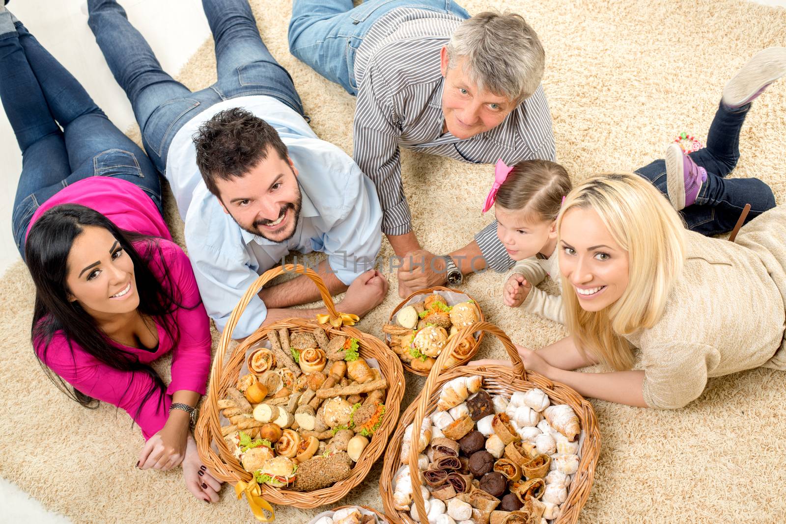 Happy family lying on a carpet in the living room around woven baskets filled with baked goods and looking at camera.