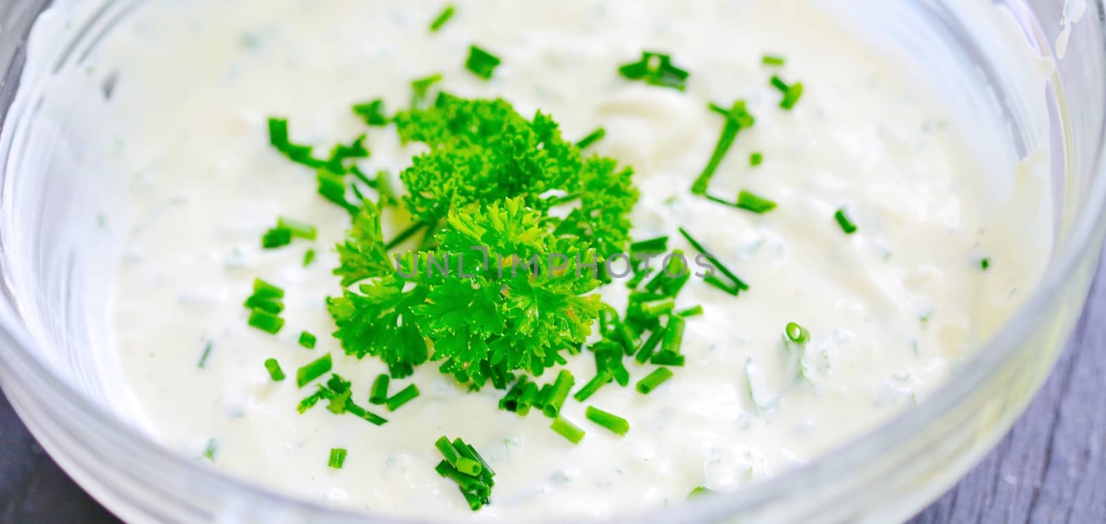 Glass bowl with garlic sour cream dressing sprinkled with fresh parsley.