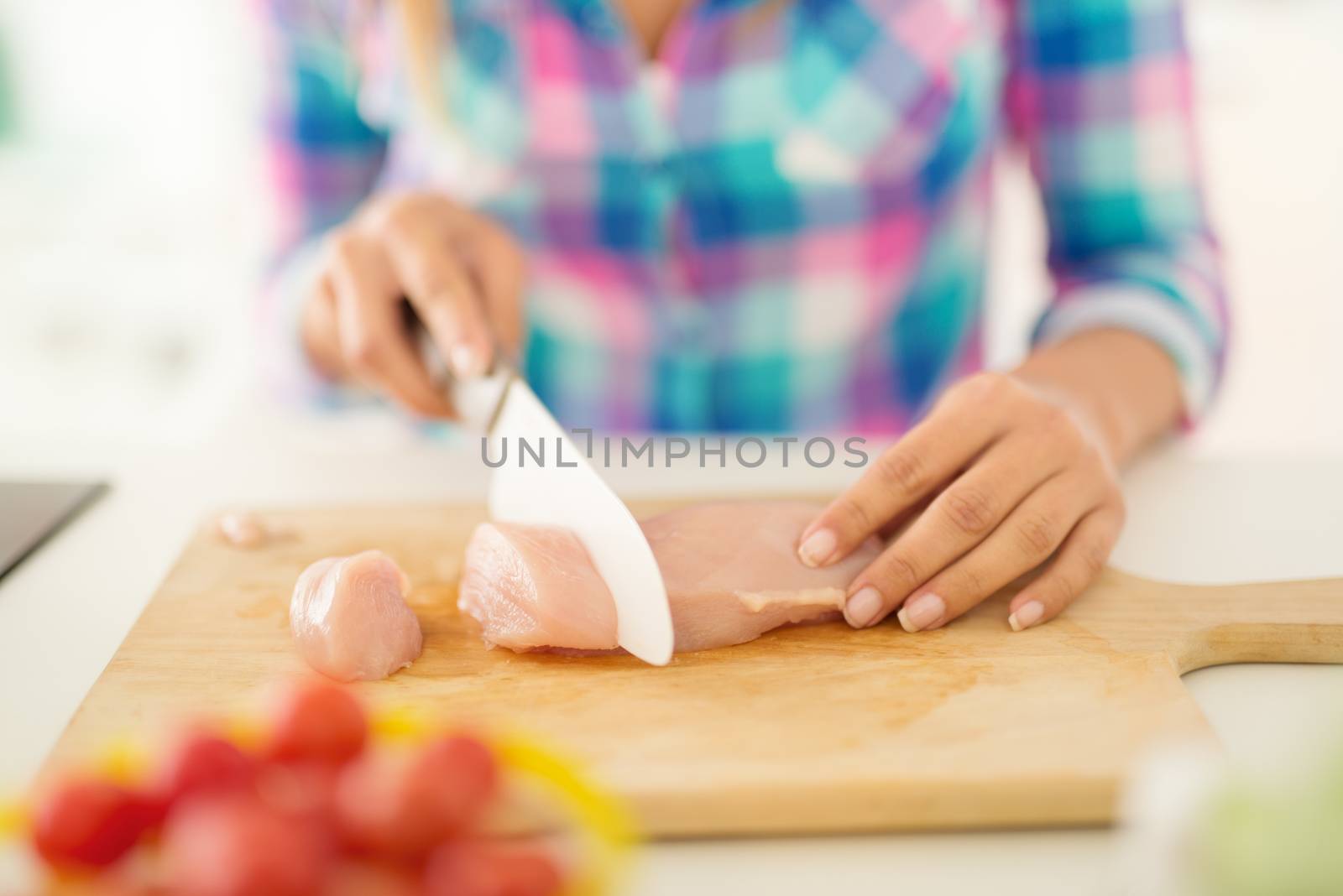 Close-up of a female hands cutting chicken filet on the kitchen board.