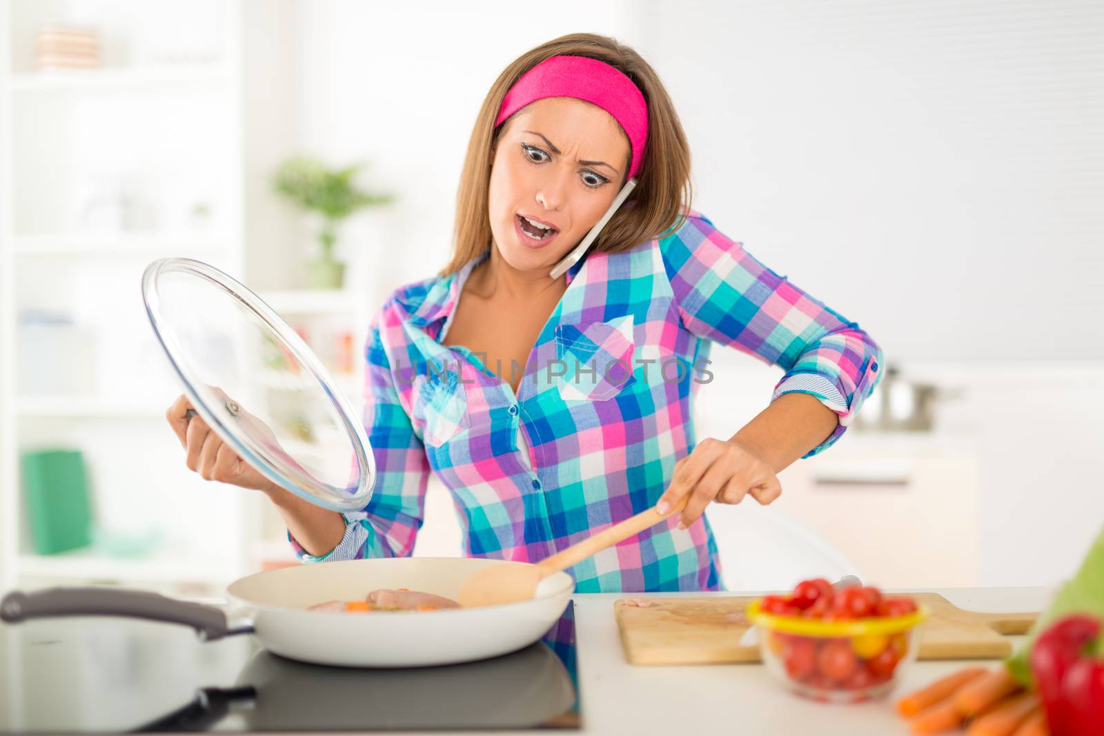 Beautiful furious young woman making healthy meal and using phone in the domestic kitchen.