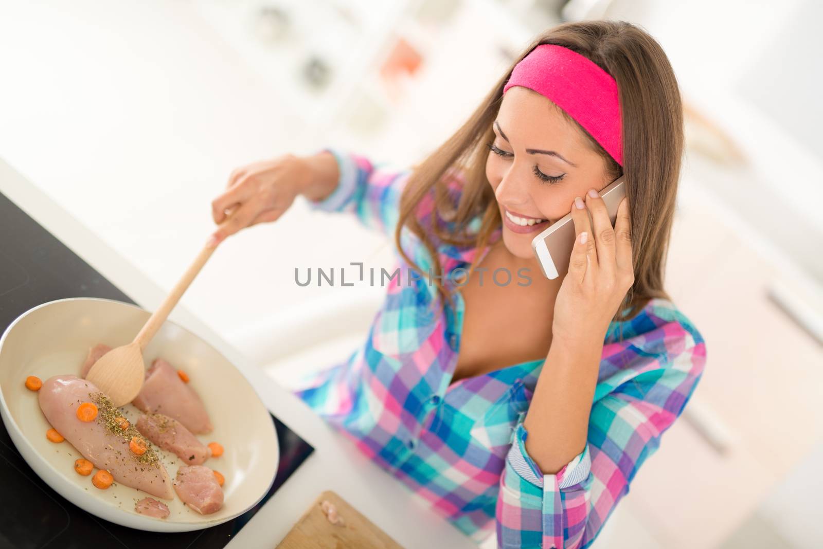 Beautiful young woman making healthy meal and using phone in the domestic kitchen.