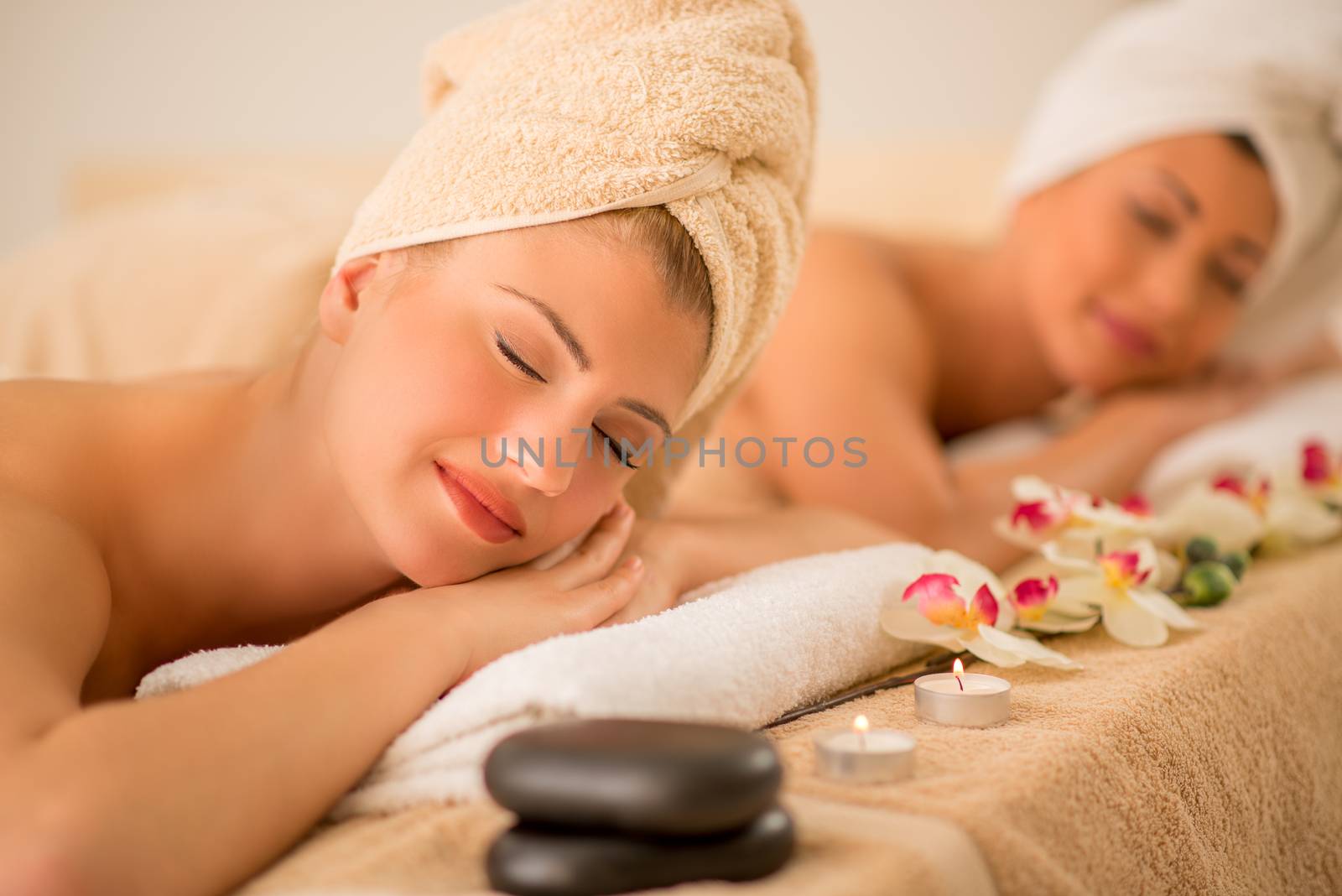 Cute young woman enjoying during a skin care treatment at a spa. Selective focus. Focus on foreground. In background her female friend relaxing.