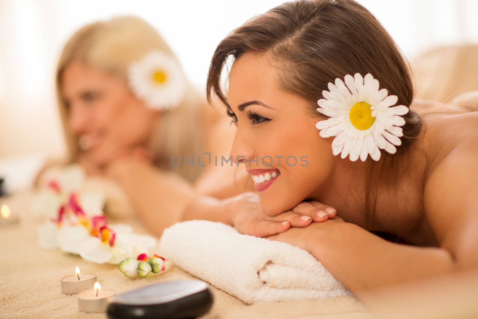 Cute young woman enjoying during a skin care treatment at a spa. Selective focus. Focus on foreground. In background her female friend relaxing.