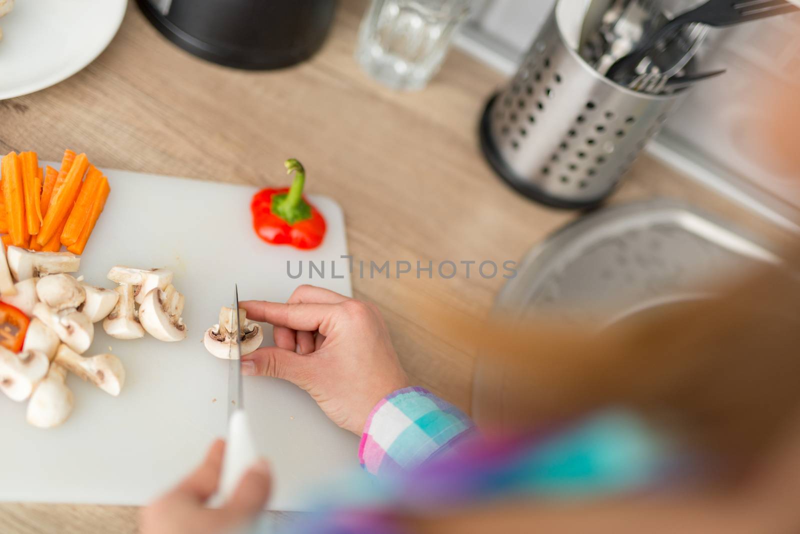 Close-up of a woman hands cutting vegetarian food on the kitchen board. Rear view.