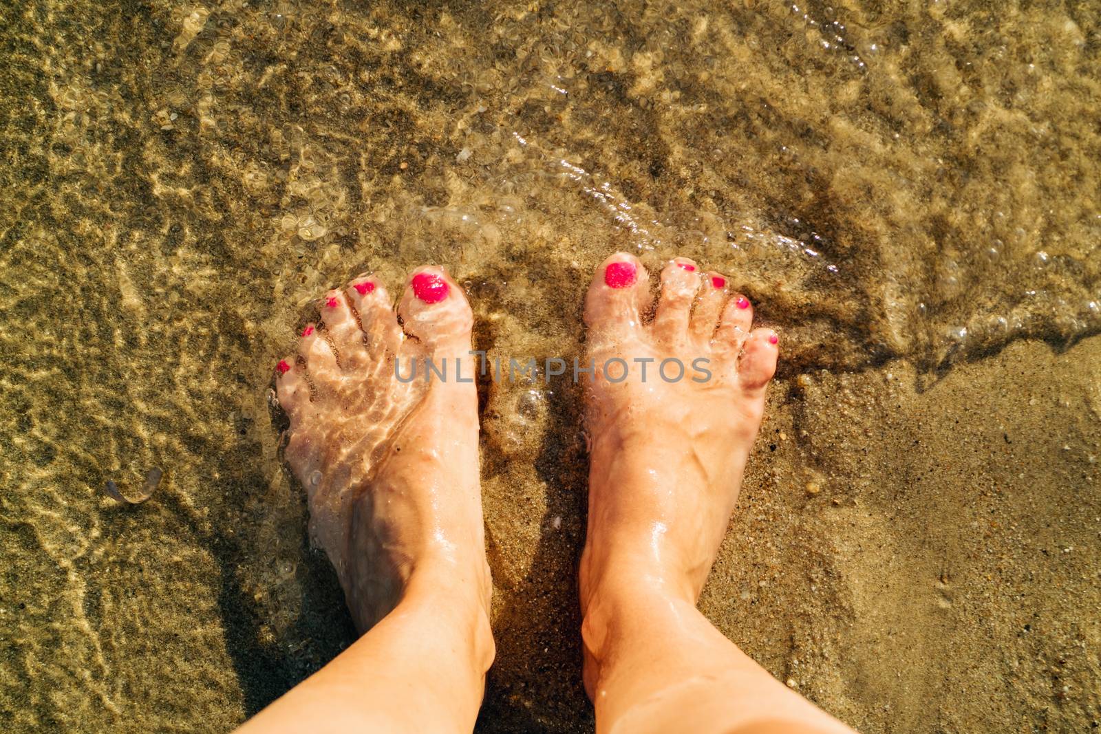 Woman standing in the coast on the sandy beach. Close-up. Focus on a foot. Top view.