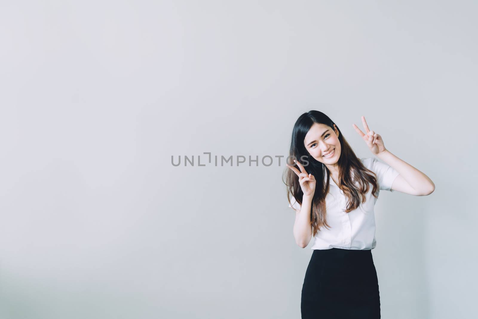 Cute asian university girl doing funny rabbit pose, copy space on gray wall background
