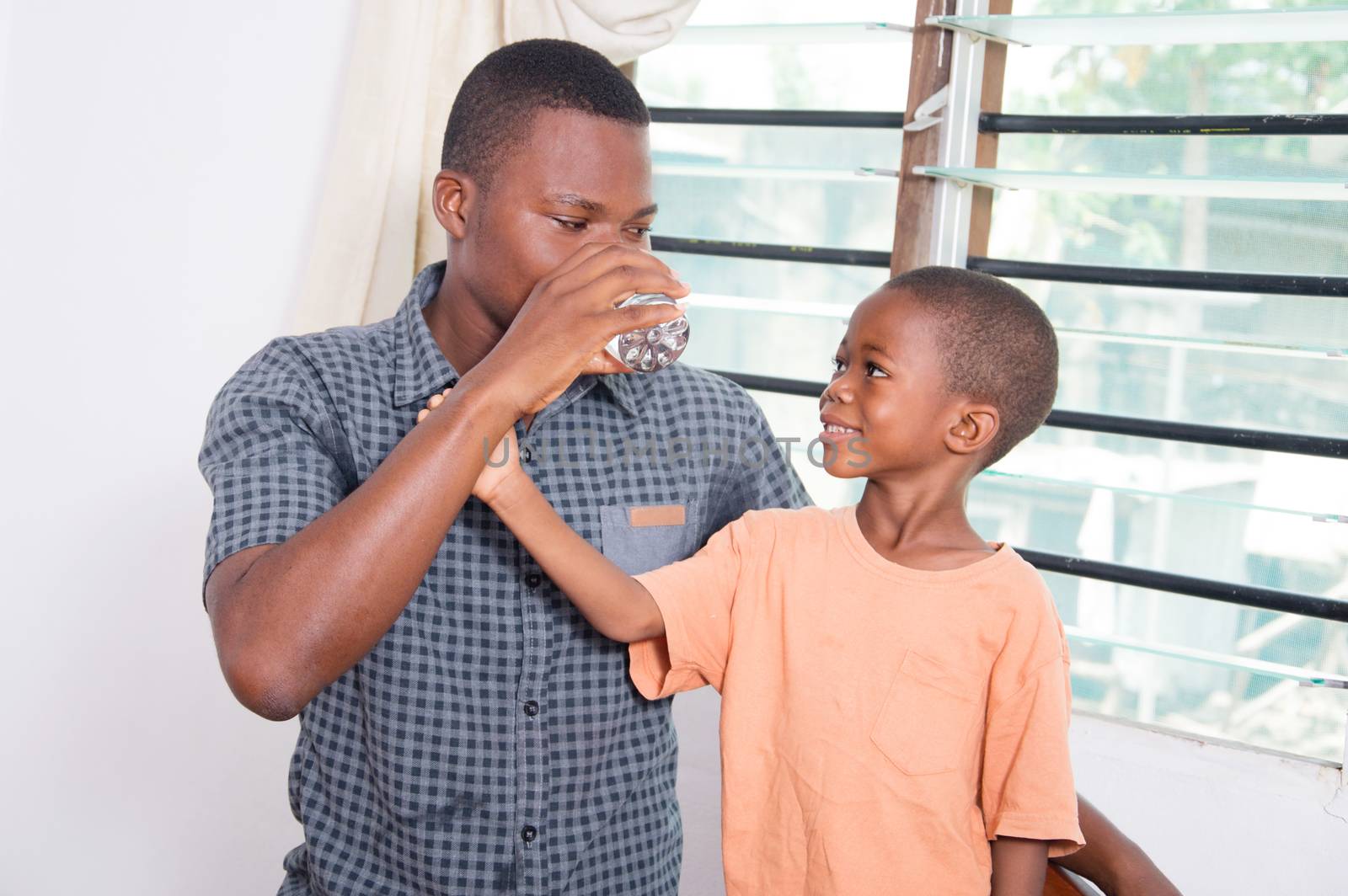 The child smiling , watching his father drink water and asked him to give him too.