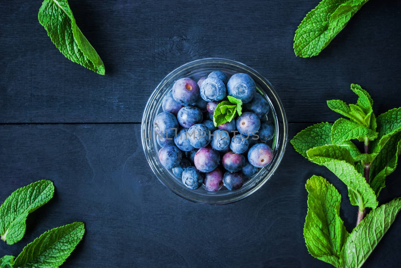 Blueberry with mint in a glass bowl on the blue wooden table