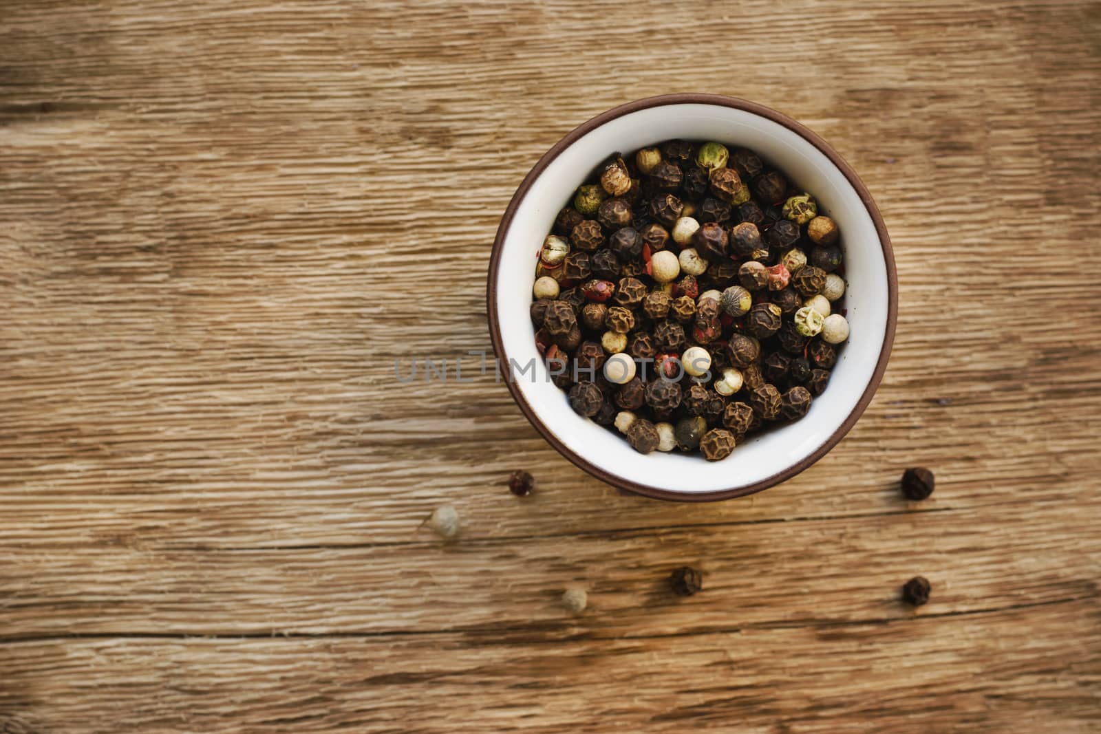 Various pepper in the ceramic dish on the wooden background