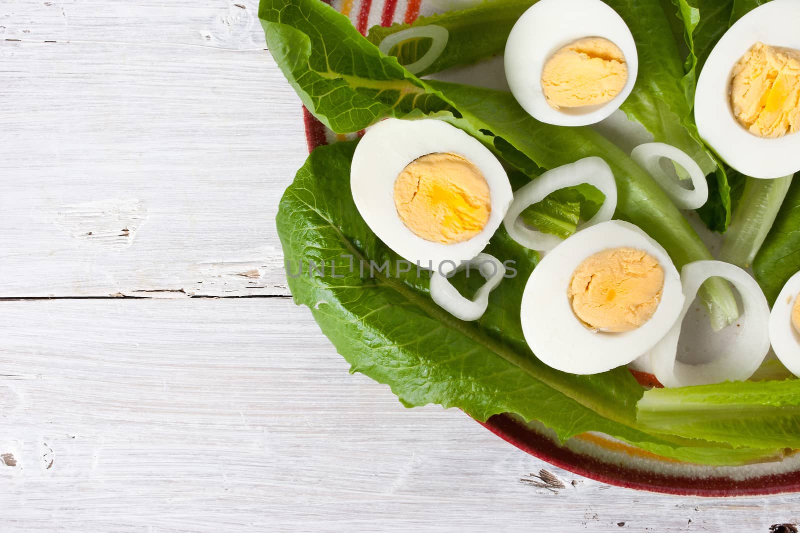Green salad with onions and eggs on the white wooden table horizontal
