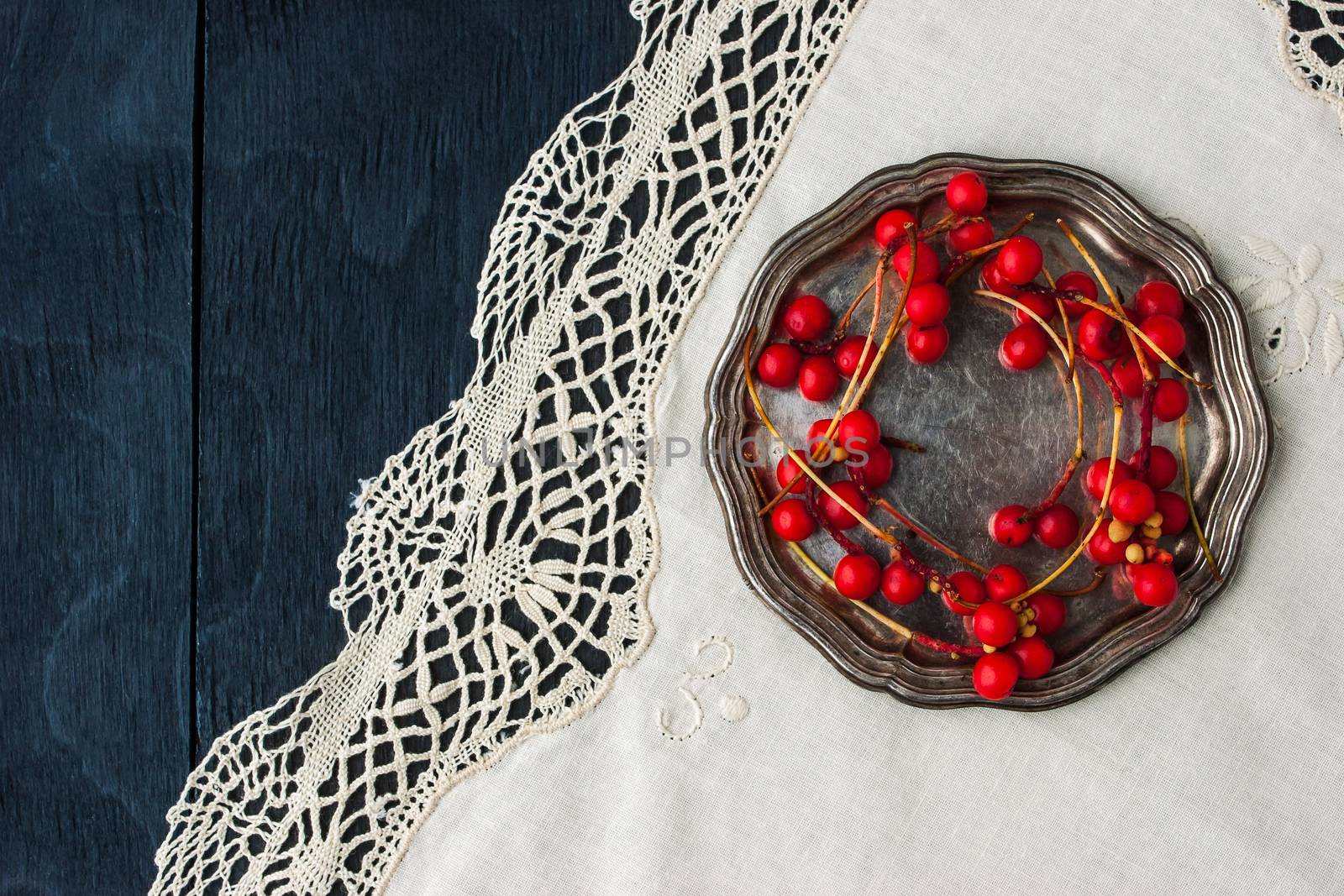 Red berries on the old metal plate on the vintage napkin top view