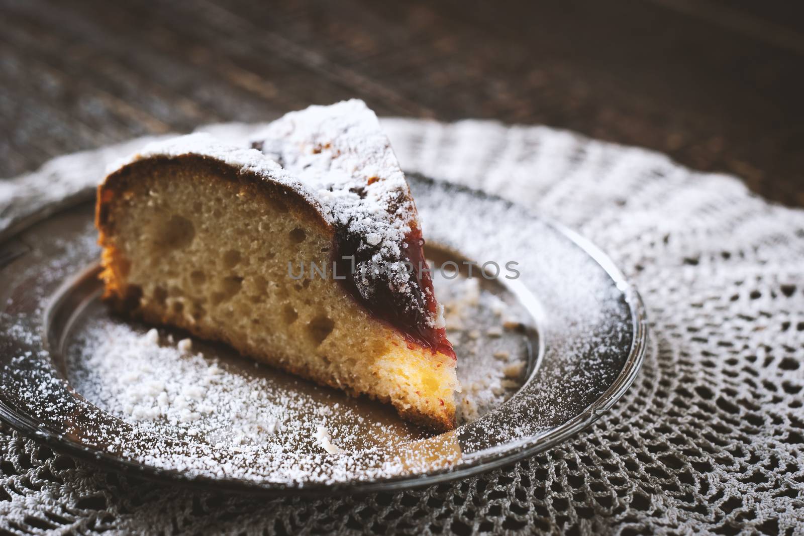 Piece of cake with icing sugar and jam on the lace napkin