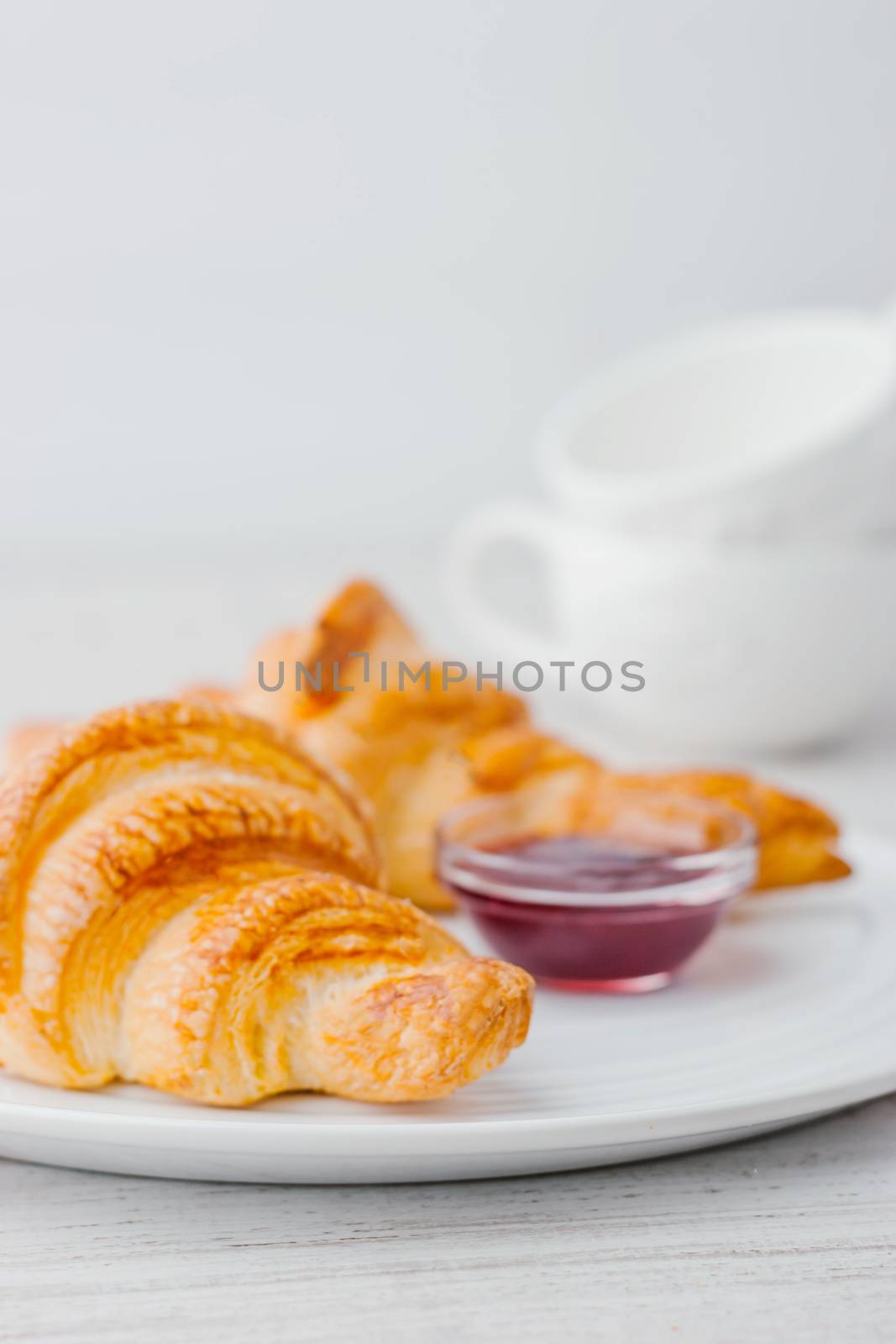 Croissants with berry jam and two white blurred cups