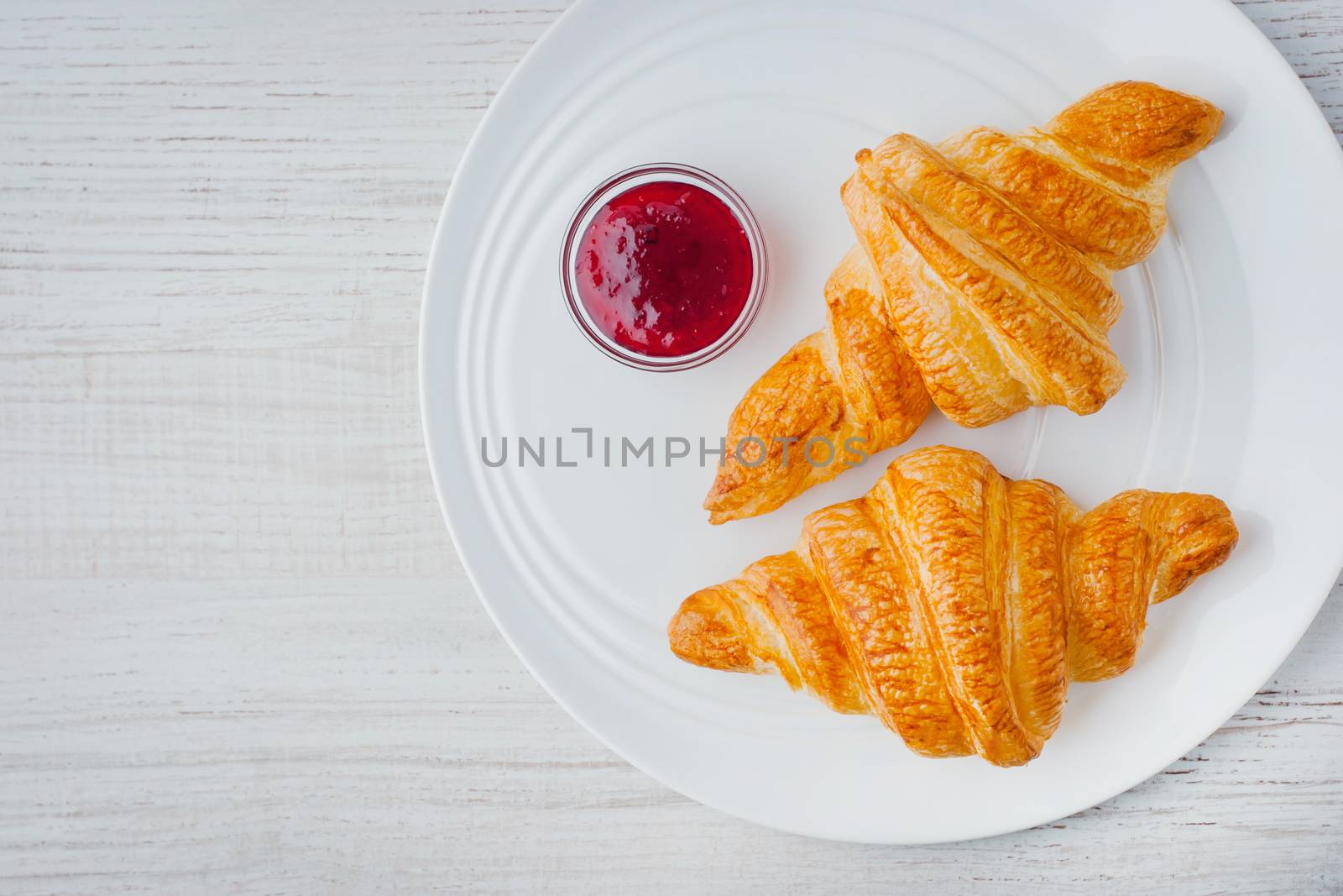 Two croissants with berry jam on the white ceramic plate top view