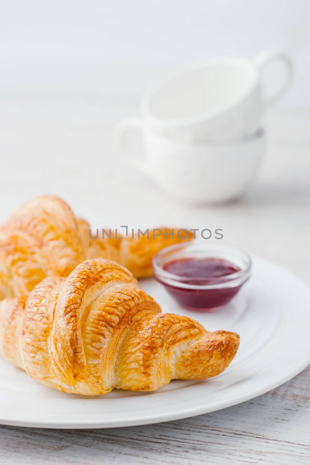 Croissants with jam and two white ceramic cups vertical