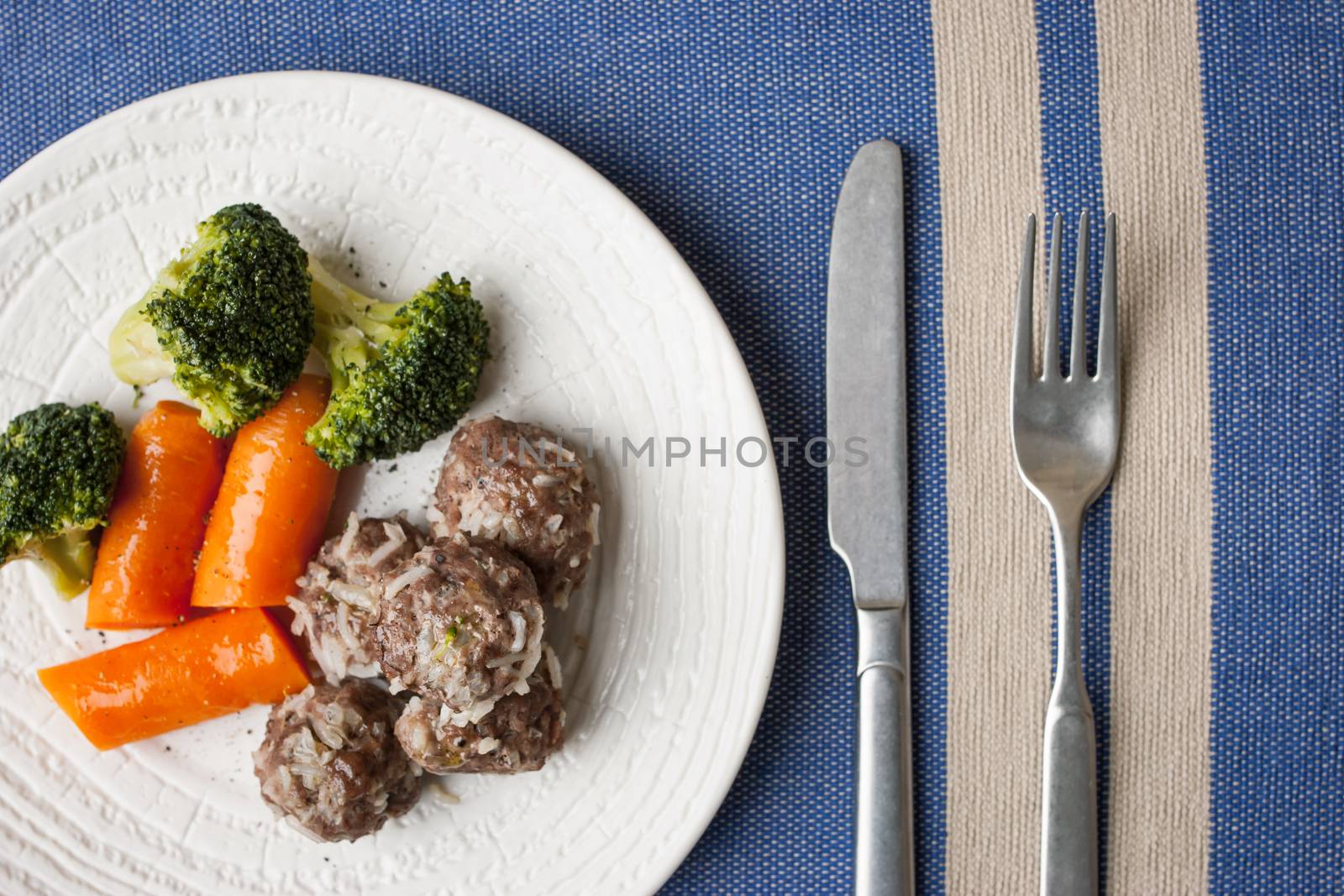 Broccoli , carrots and meatballs on the blue napkin with cutlery top view