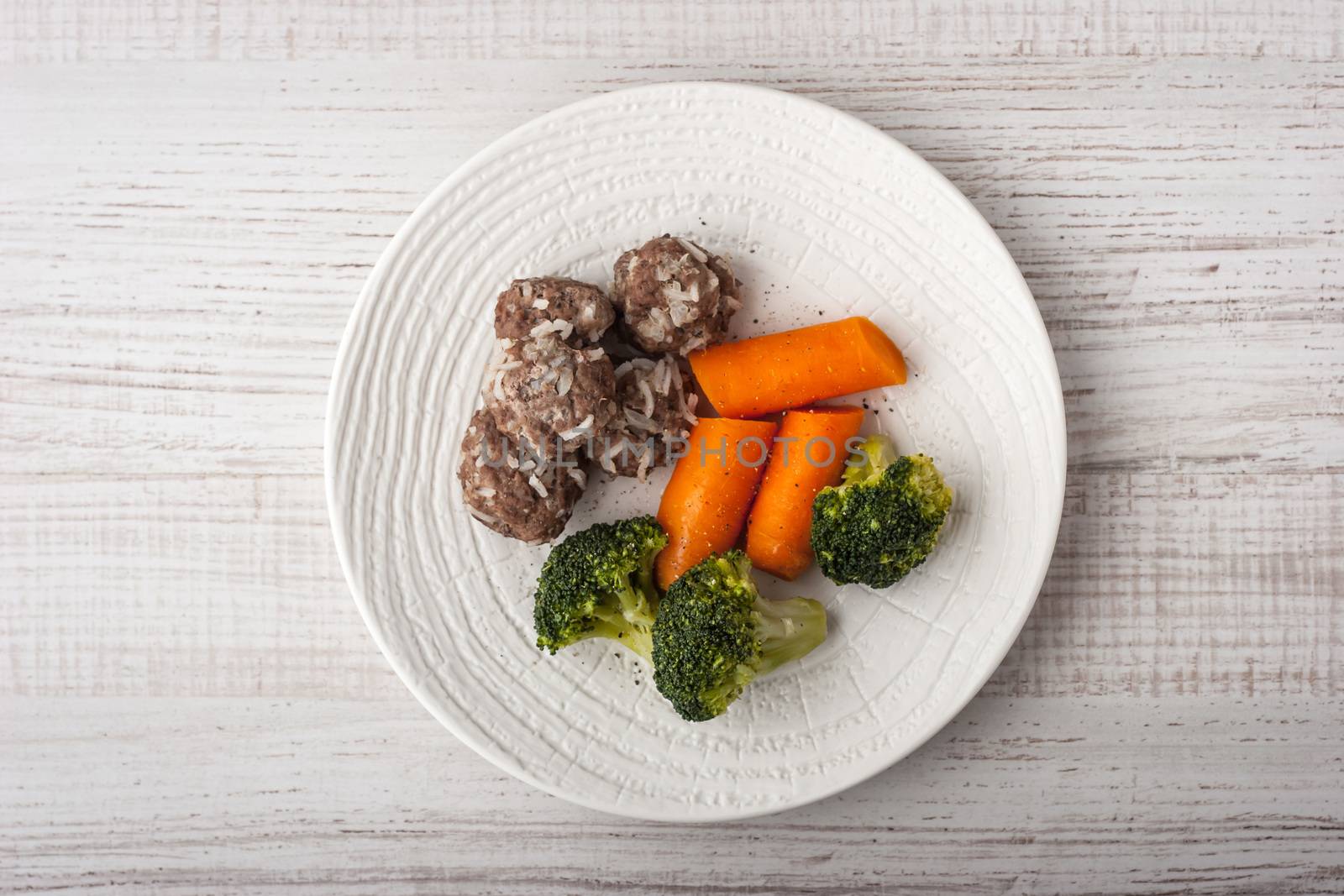 Steamed broccoli and carrots with meatballs on the white plate top view