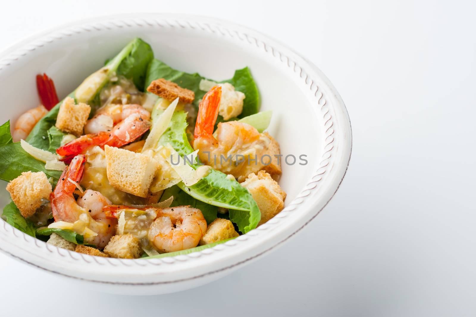 Caesar salad with prawns on the white plate horizontal