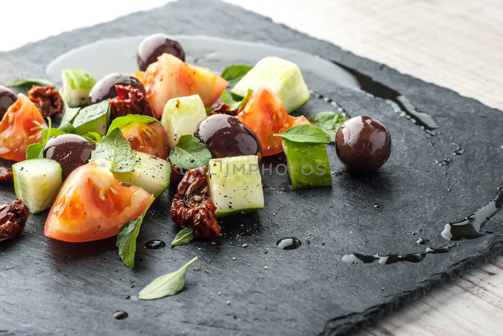 Salad with fresh and dried tomato and olives on the black stone close-up