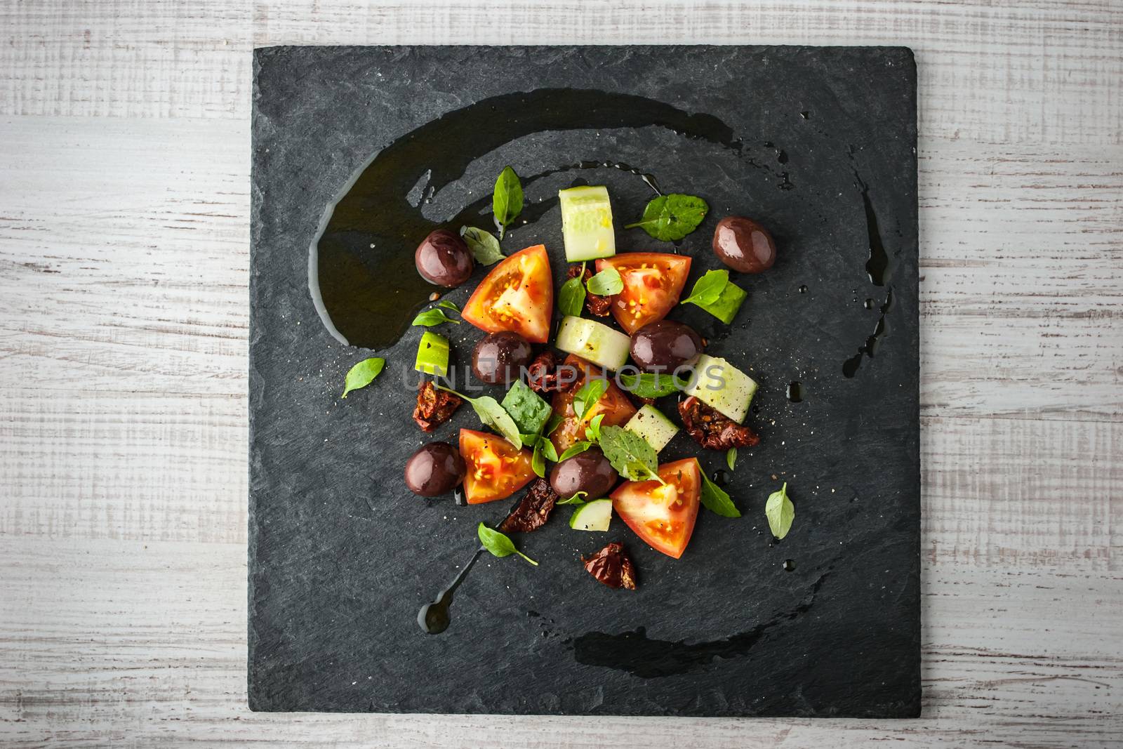 Vegetable salad with dried tomatoes and olive on the black stone top view
