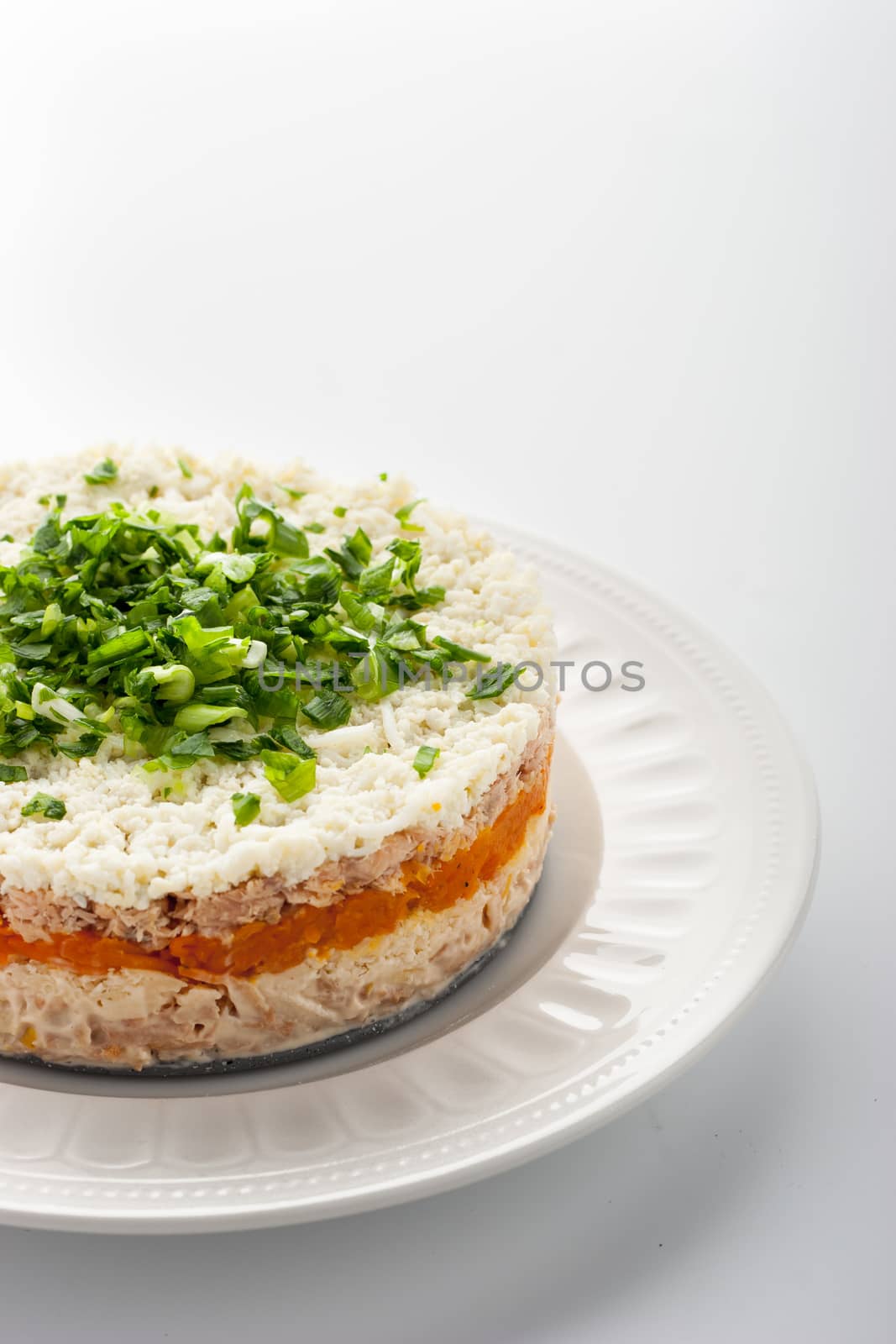 Layered salad with eggs and fish on the white ceramic plate vertical