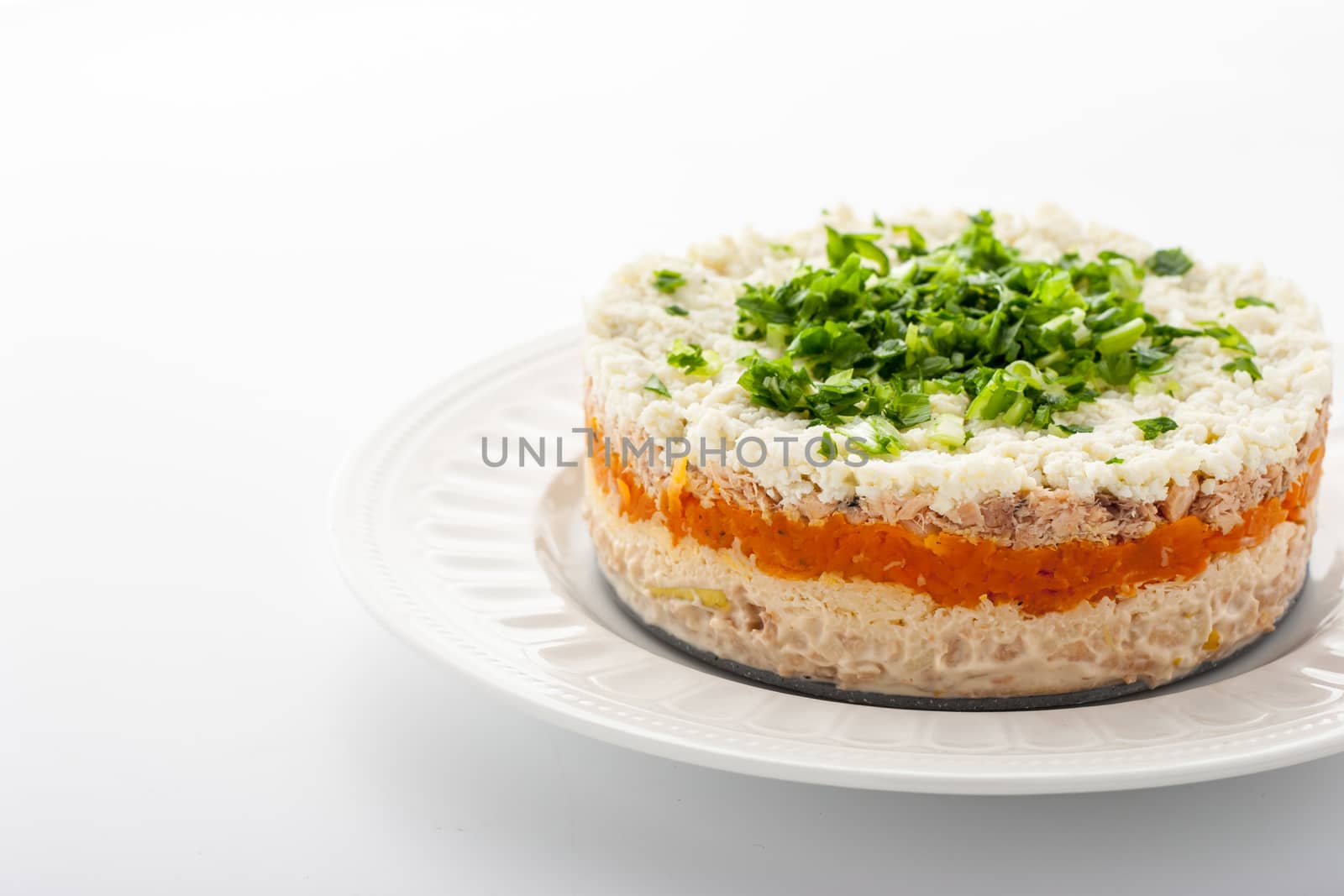 Layered salad with eggs and fish on the white ceramic plate horizontal