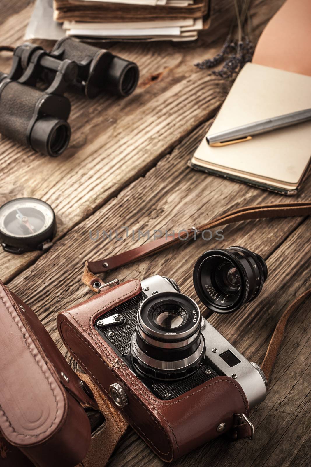 Camera with notebook and binoculars on the wooden table vertical