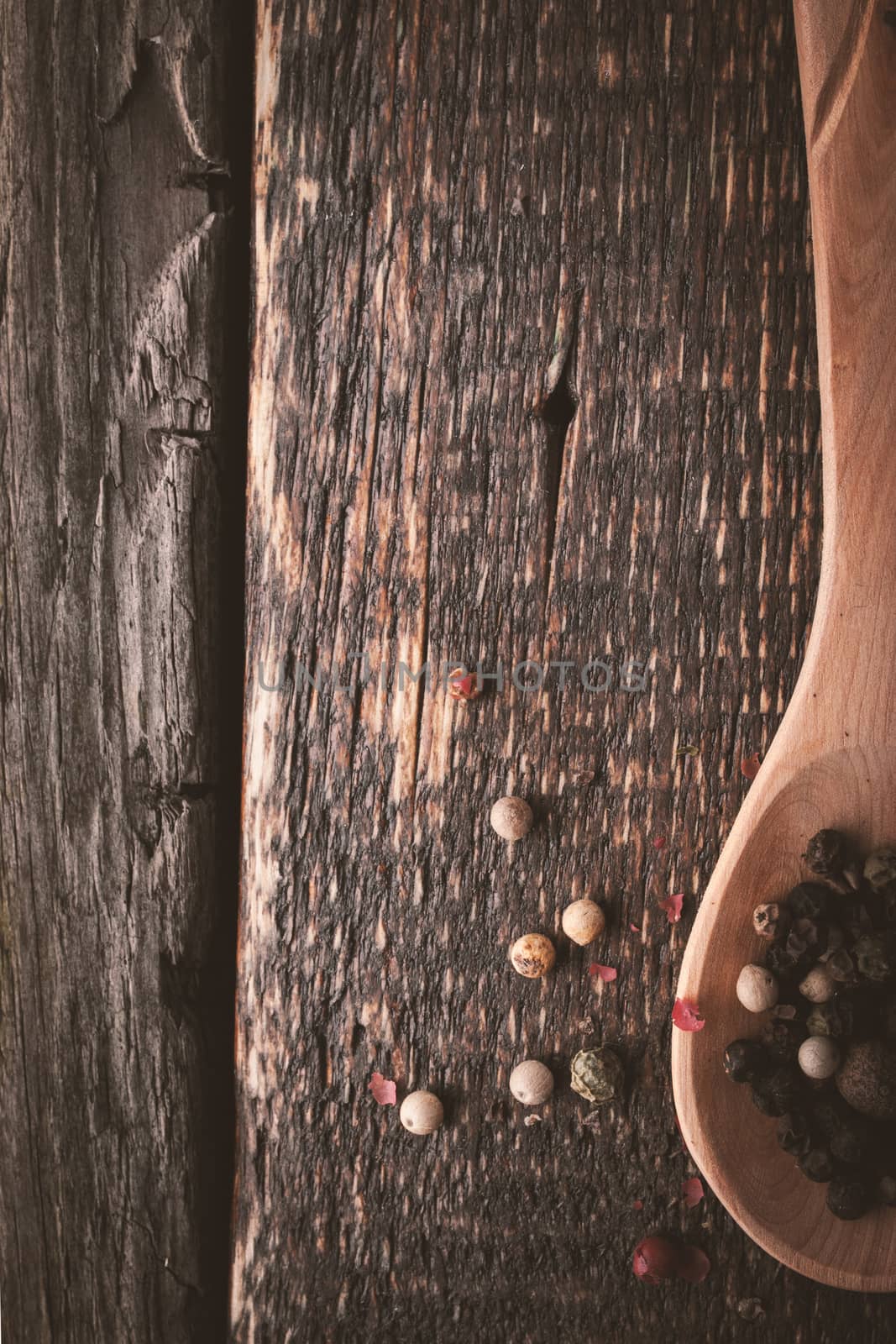 Wooden spoon with pepper mix on the wooden background vertical