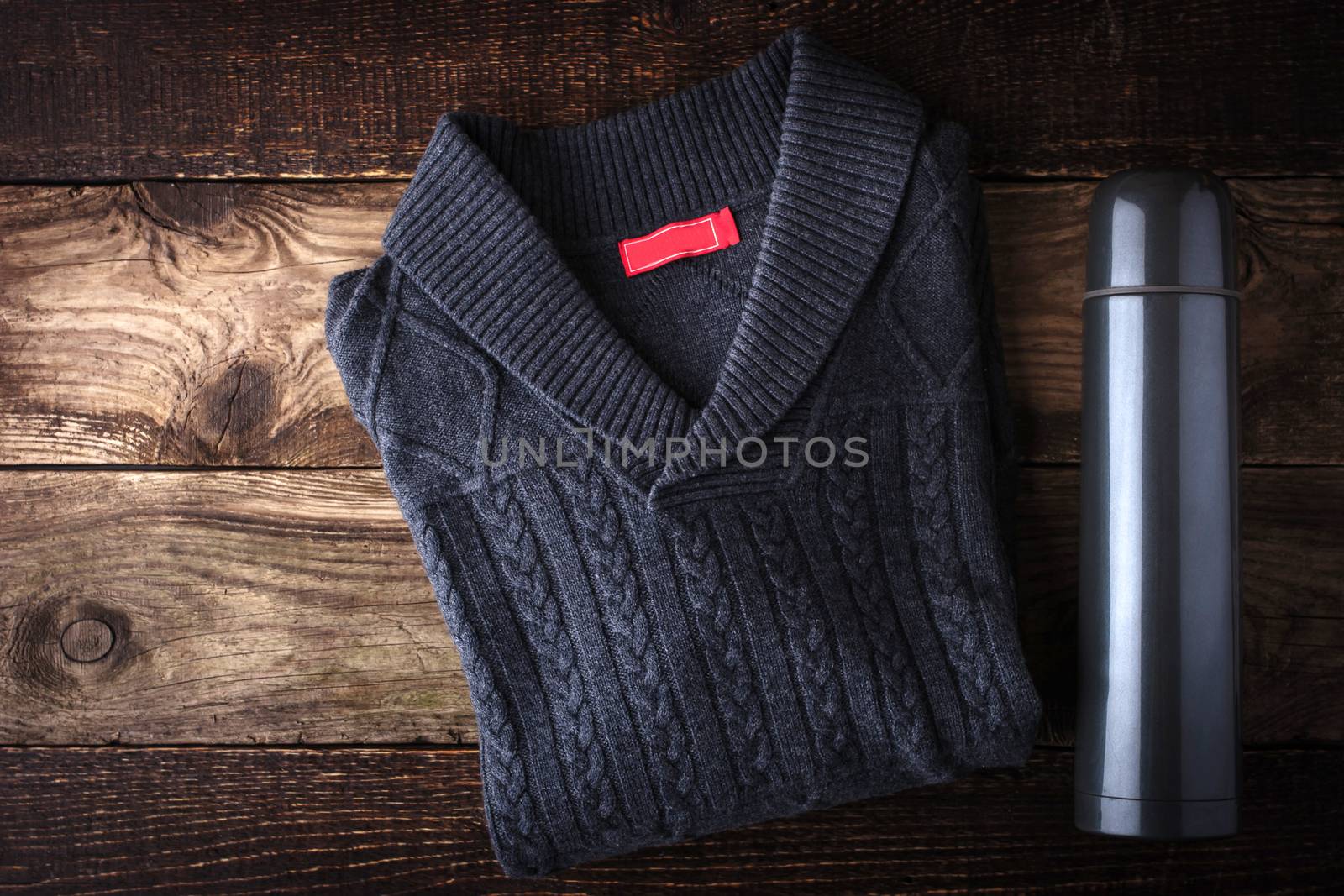 Grey sweater and thermos on the wooden background