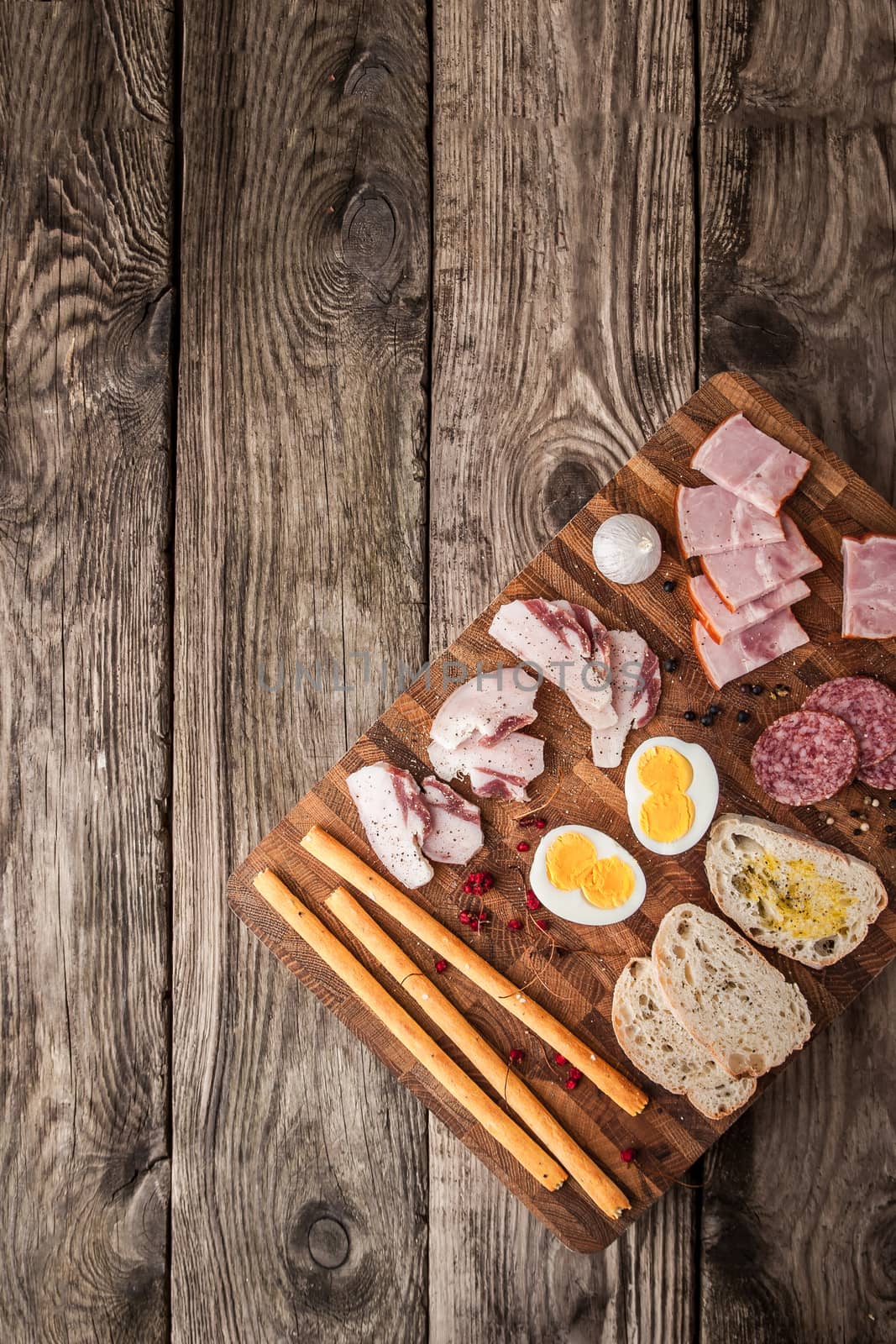 Eggs, ham, sausage, bread, pepper, garlic on a cutting board vertical