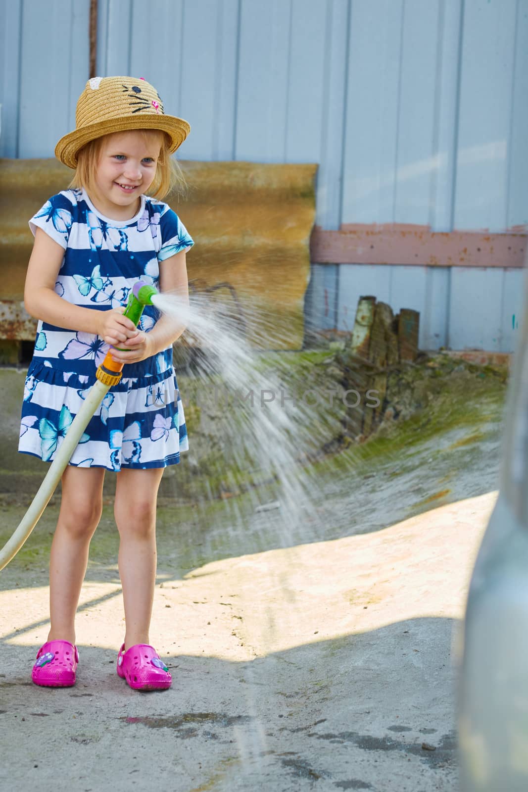 Little girl in hat watering lawn. Summer day