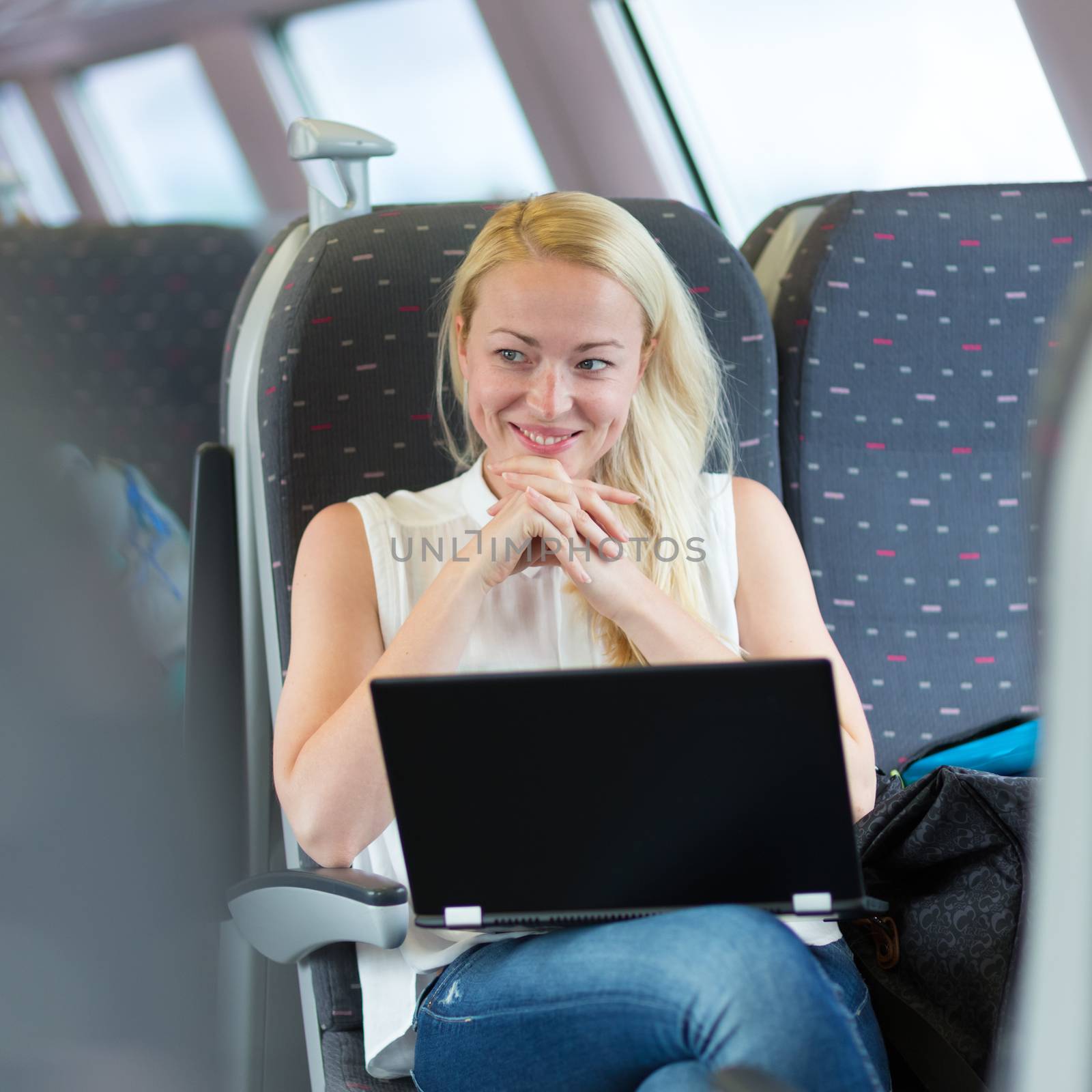 Woman traveling by train smiling and flirting while working on laptop.
