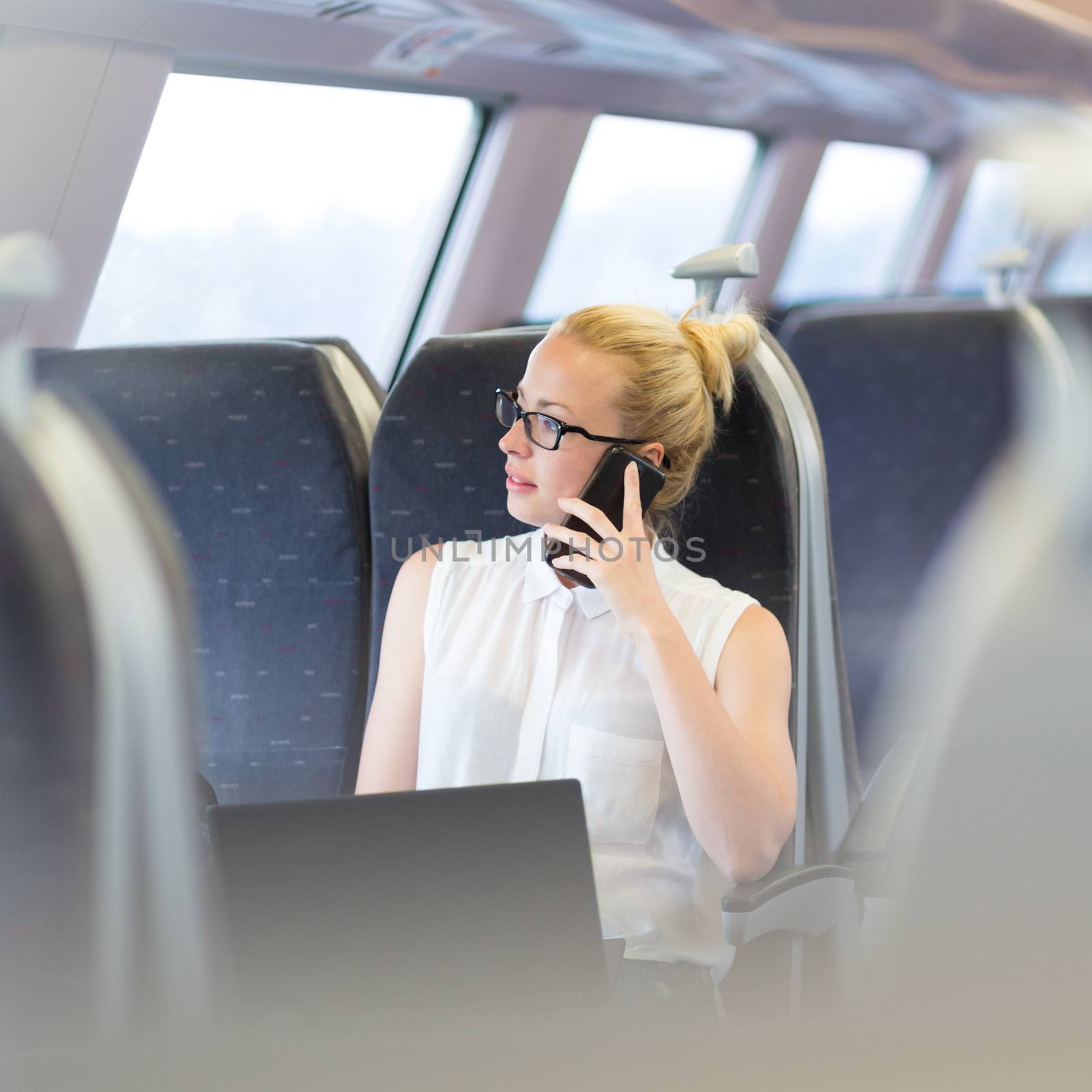 Businesswoman talking on cellphone and working on laptop while traveling by train. Business travel concept.