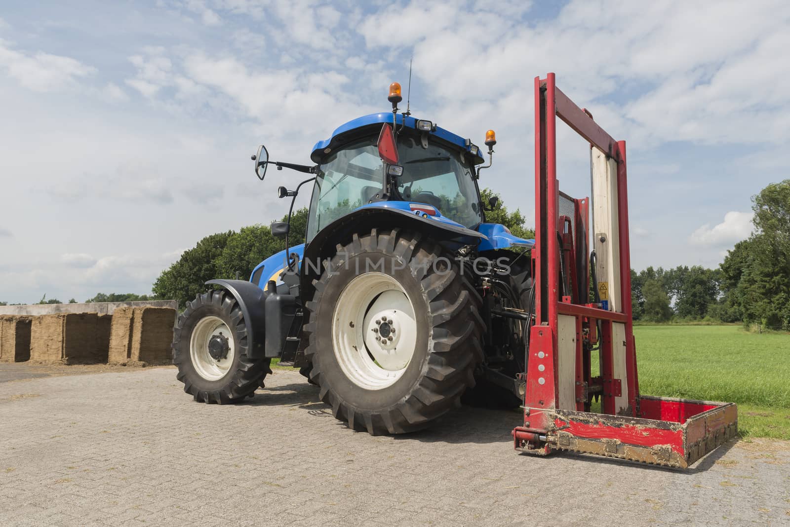 Blue tractor with a red bale slicer for cutting off silage bales
