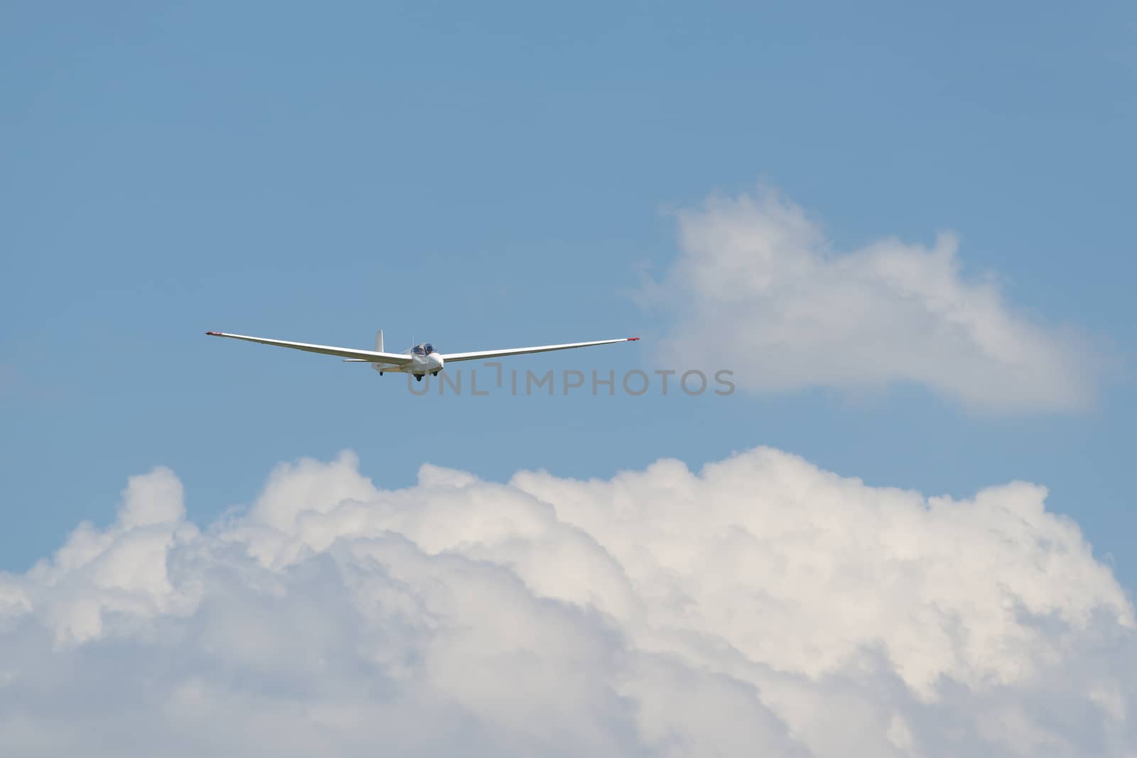 Glider above white clouds against a blue sky as background picture for extreme sports
