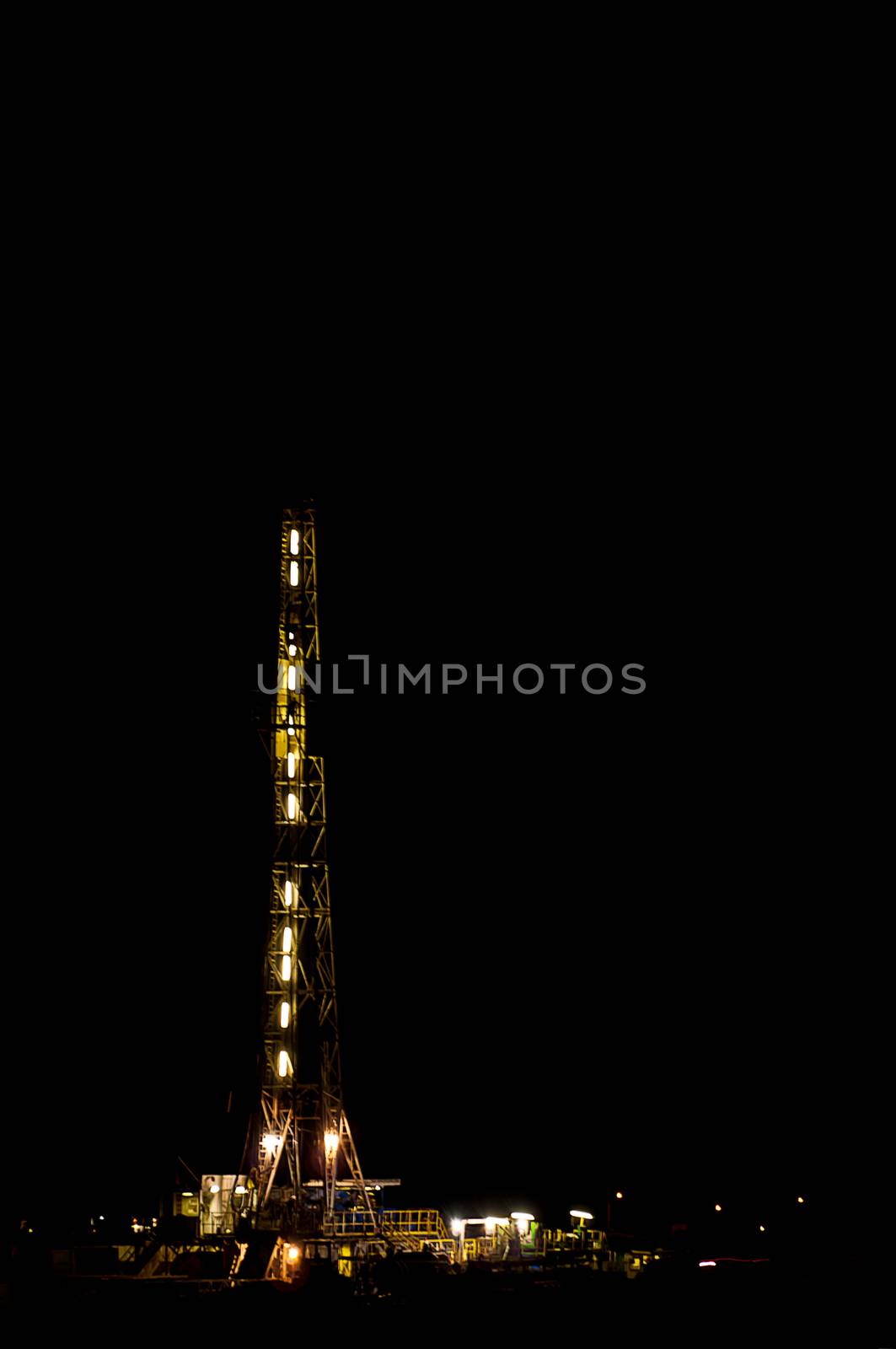 Oil rig lit up on a moonless night drilling around the clock in a producing oil and gas field