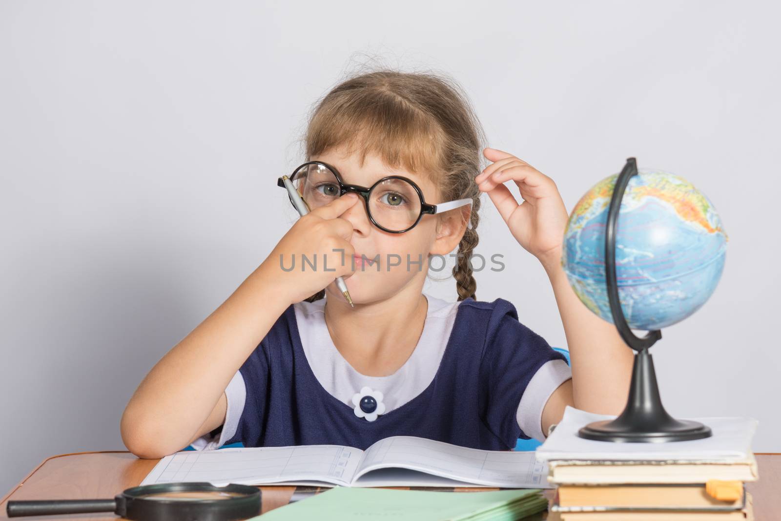 Schoolgirl corrects glasses while sitting at a desk in the classroom Geography