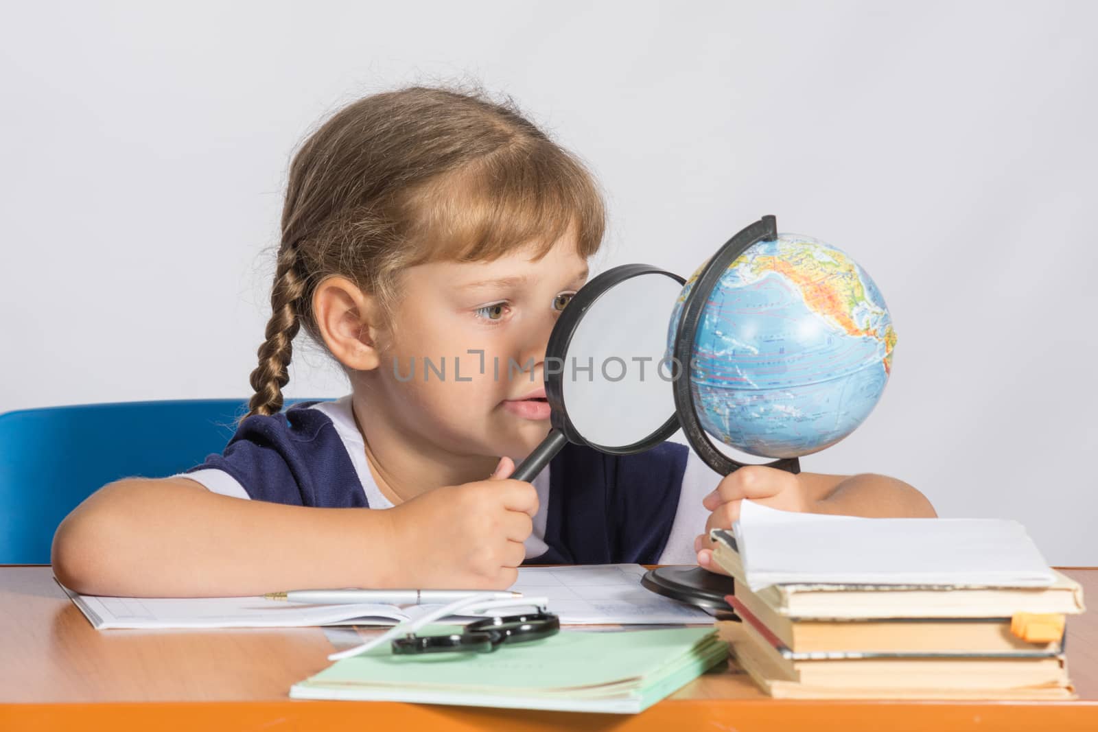 Six-year girl sitting at the table and looks at the globe through a magnifying glass