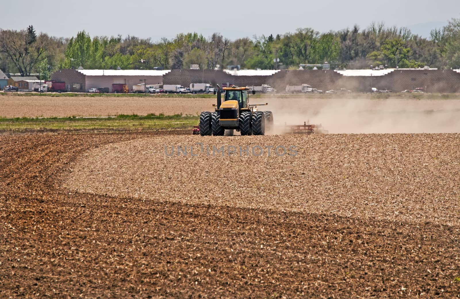 Farmer in a large tractor pulling a disc harrow through his field to break up the soil for spring planting.