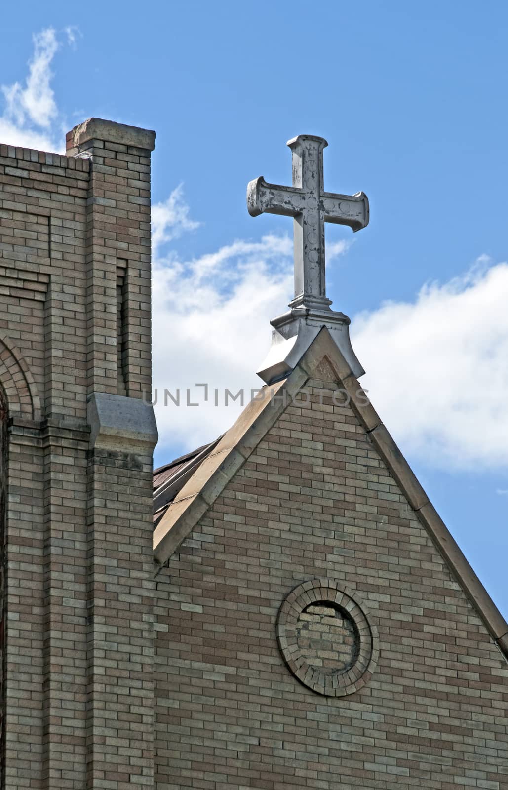 Iron cross on top of a Christain church steeple against a blue sky.