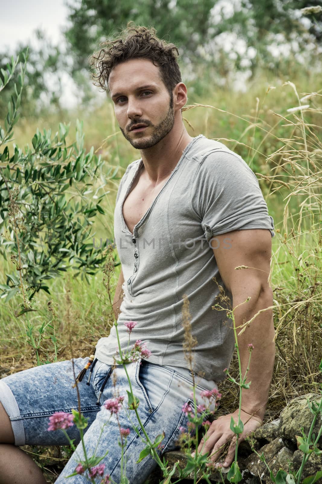 Good looking male model sitting on grass in a field, looking at camera