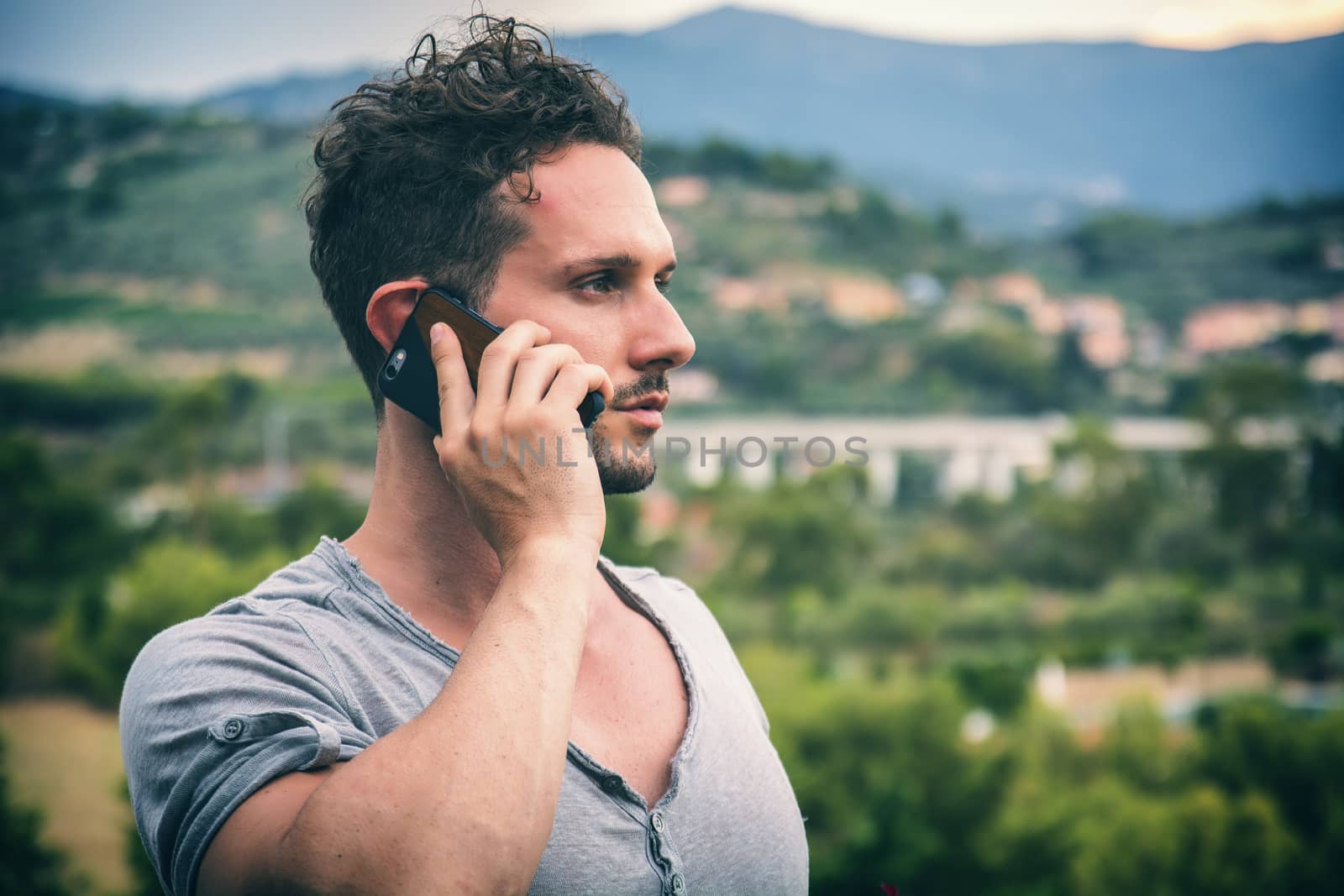 Handsome man doing a phone call, talking on cell phone, standing outdoor during daytime